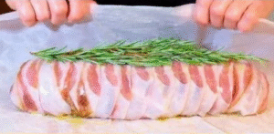 Preparing the stuffed turkey roll recipe wrapped in bacon and rosemary before baking.