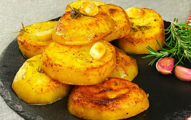 golden garlic butter potatoes with garlic cloves and rosemary on black plate