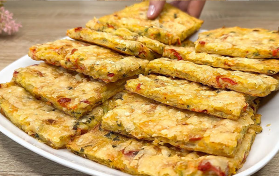 Baked potato squares with melted cheese and vegetables on a white plate.