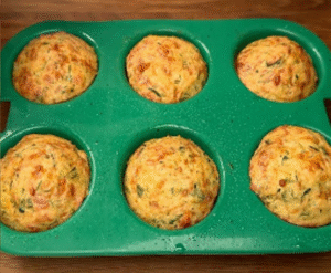 Unbaked zucchini muffins recipe in a tray, filled with grated zucchini, potatoes, cheese, and herbs, ready to go into the oven.