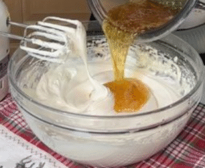Pouring hot honey into glossy whipped egg whites for homemade white nougat recipe.