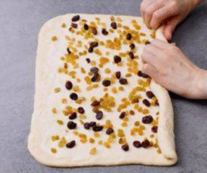 Rolling out brioche dough and sprinkling raisins and cranberries evenly on top.