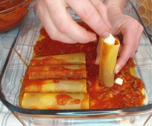 Filling cannelloni tubes with ragù and cheese over tomato sauce