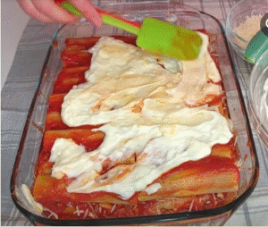 Spreading creamy béchamel over stuffed cannelloni