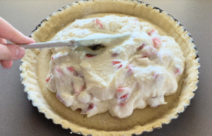 Spreading ricotta and strawberry cream inside the tart crust.