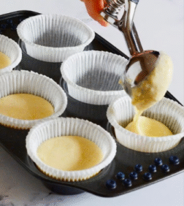 Batter being poured into muffin cups for a cream muffin recipe