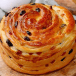 Freshly baked raisin brioche recipe with a golden swirl and glossy surface.