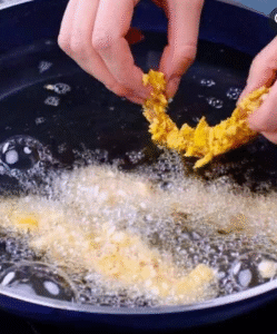 hands dipping chicken strips into crushed cornflakes before frying in hot oil