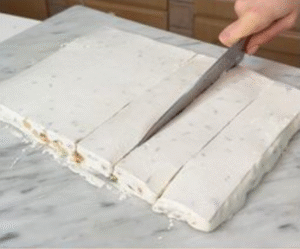 White nougat slab being sliced into equal bars.