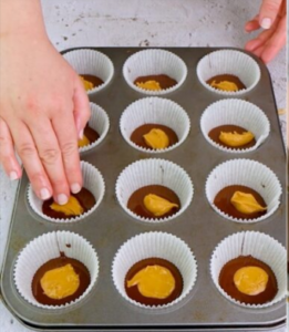 Filling cupcake liners with melted chocolate and peanut butter to make homemade chocolate peanut butter cups.