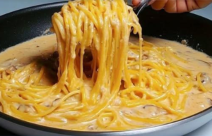 cooking creamy mushroom spaghetti with melted cheese in a pan