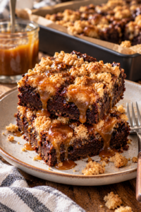 Stacked caramel brownie bars with fudgy chocolate centers, golden crumbs, and glossy caramel sauce.