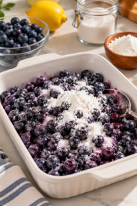Blueberry crisp with frozen blueberries in the preparation stage with sugared frozen blueberries in a white baking dish.