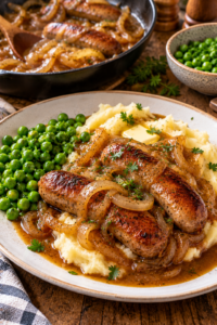 Finished bangers and mash with onion gravy, creamy potatoes, and green peas.