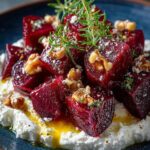 Roasted beet salad with whipped feta, walnuts, and fresh herbs on a dark plate.