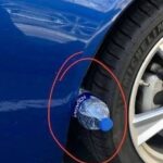 Water Bottle on Car Tire wedged between a blue vehicle’s tire and wheel arch