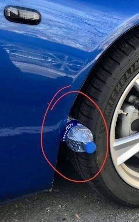 Water Bottle on Car Tire wedged between a blue vehicle’s tire and wheel arch