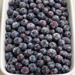 Blueberry crisp with frozen blueberries prepared in a white baking dish before adding the oat topping.