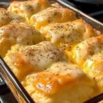 Cheesy garlic dinner rolls baked in a glass dish with golden tops, melted cheese, and herbs.