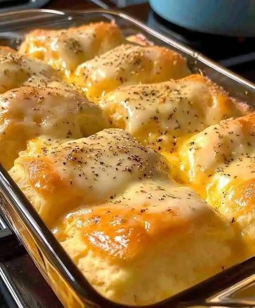 Cheesy garlic dinner rolls baked in a glass dish with golden tops, melted cheese, and herbs.