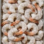 Frozen raw peeled shrimp with tails arranged on a metal tray before making garlic butter shrimp.