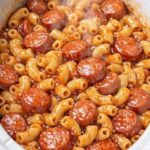 Slow cooker sausage pasta with elbow macaroni and sliced smoked sausage coated in tomato sauce.