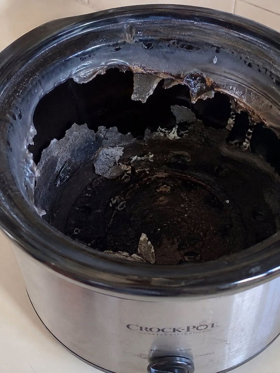 Cracked slow cooker insert with large broken areas and loose ceramic fragments