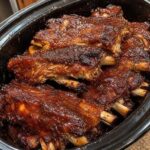 Slow cooker BBQ ribs coated in a glossy barbecue glaze, with browned edges and visible bones.