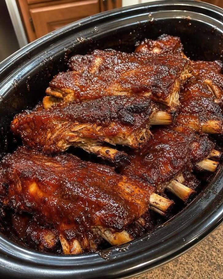 Slow cooker BBQ ribs coated in a glossy barbecue glaze, with browned edges and visible bones.