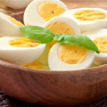 Perfect Hard Boiled Eggs halved in a wooden bowl with fresh basil garnish