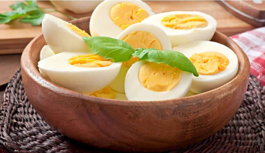 Perfect Hard Boiled Eggs halved in a wooden bowl with fresh basil garnish