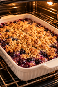 Blueberry crisp with frozen blueberries baking in a white dish with a golden oat topping and bubbling berry filling.