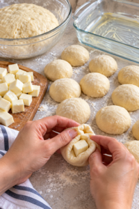 Mozzarella cube being wrapped in dough to make cheesy garlic dinner rolls
