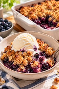 Blueberry crisp with frozen blueberries served warm in a bowl with vanilla ice cream.