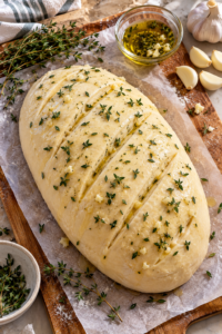 Scored unbaked garlic herb bread dough topped with fresh thyme