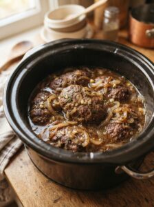 Salisbury steak patties and onions cooking in gravy for Slow Cooker Salisbury Steak.