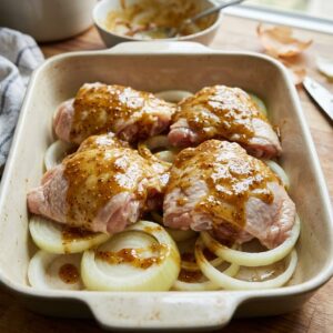 Chicken thighs coated in sauce over onion rings for 3-Ingredient Charleston Chicken before baking.